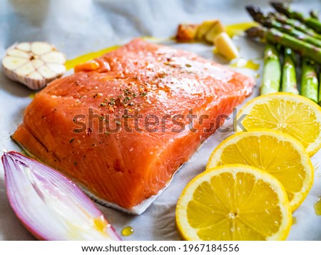 Fresh raw salmon steak with asparagus, cherry tomatoes, lemon, garlic and onion on cooking pan prepared to roast