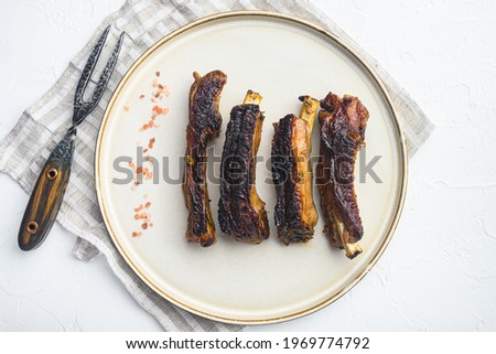 Grilled pork rib set, on plate, with barbeque knife and meat fork, on white stone background, top view flat lay
