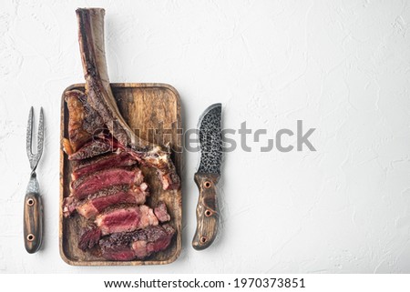 Grilled sliced tomahawk beef steak set, on wooden serving board, on white stone background, top view flat lay, with copy space for text
