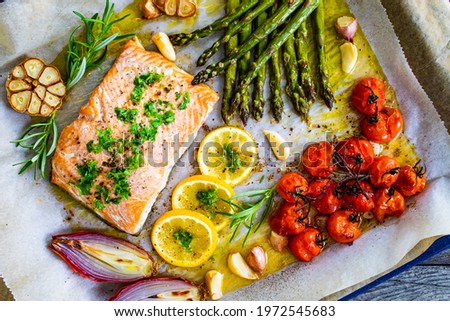 Sheet pan dinner - roasted salmon steak with asparagus, lemon ,rosemary, tomatoes, onion and garlic on cooking pan on wooden table 