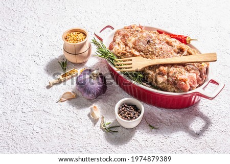 Raw pork roll stuffed with garlic and carrots in a ceramic roasting dish. Fresh meat, spices, rosemary, garlic. Light putty background, modern hard light, dark shadow, copy space