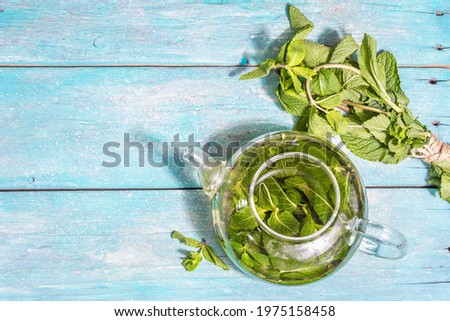 Mint tea from fresh leaves. Healthy hot drink in a glass teapot. Modern hard light, dark shadow, turquoise wooden boards background, top view