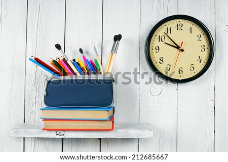 Clock, books and school tools on a wooden shelf. On a white, wooden background.