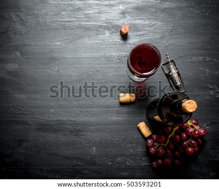 Bouteille de vin rouge avec tire-bouchon. Sur fond noir bois.