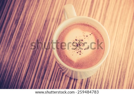 heart pattern in a cup of coffee on wooden background - vintage style effect picture