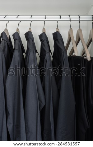 row of black shirts and pants hanging on coat hanger in white wardrobe