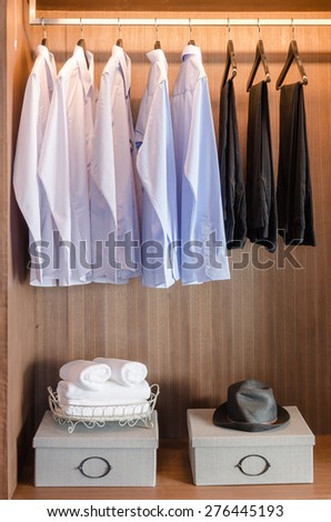 shirts and pants hanging  on rack in wooden wardrobe with boxes on shelf