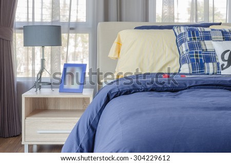 blue picture frame with modern lamp on wooden side table and blue bed with yellow pillow