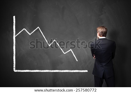 businessman standing in front of a decreasing chart on a blackboard
