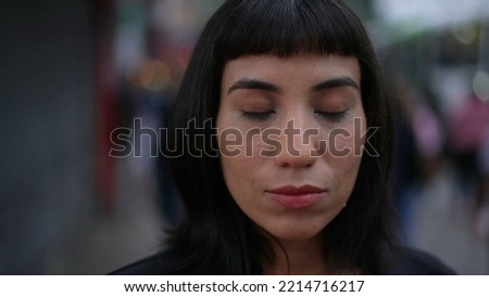 Contemplative young hispanic woman closing eyes in street. South American adult person with indigenous traits opening eye smiling. Portrait face closeup in urban environment Foto stock © 