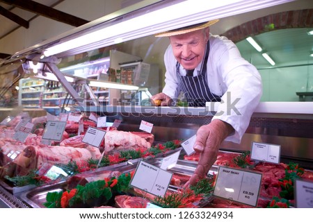 Butcher in apron and hat arranging display of meat in shop chiller Stockfoto © 