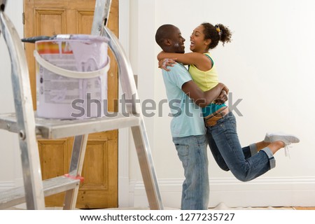 Loving couple decorating room with paint pot and ladder