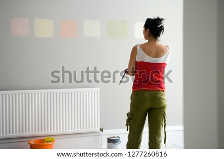 DIY woman choosing paint color swatches on room wall deciding on decor for home improvement