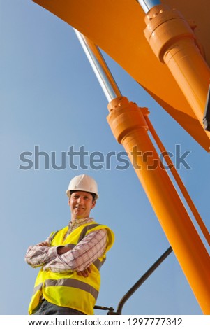 Construction worker in hard hat with plant machinery smiling at camera