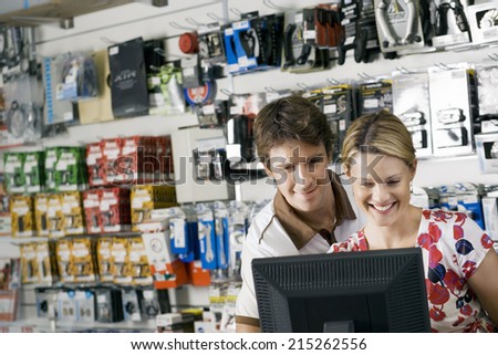 Young couple looking at visual screen beside bike accessories display rack in bicycle shop, smiling
