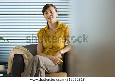 Businesswoman in yellow short-sleeved blouse sitting in office chair, smiling, portrait