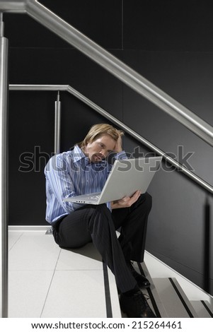 Businessman sitting on staircase, using laptop in lap, leaning head on hand, thinking, side view