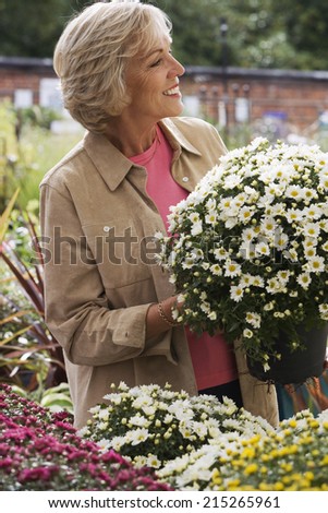 Senior woman shopping for flowers in garden centre, holding pot plant, smiling, side view