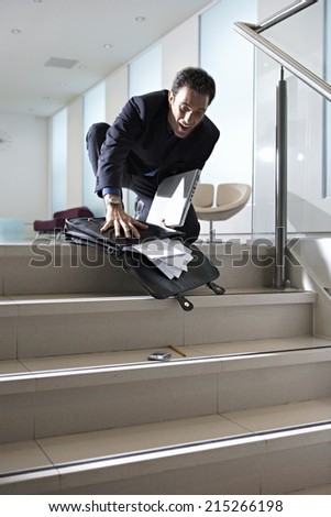 Businessman dropping briefcase on steps in office lobby, contents spilling onto floor, low angle