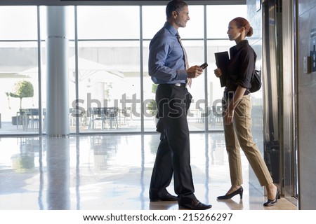Businesswoman and businessman standing beside elevator in lobby, face to face, talking, profile