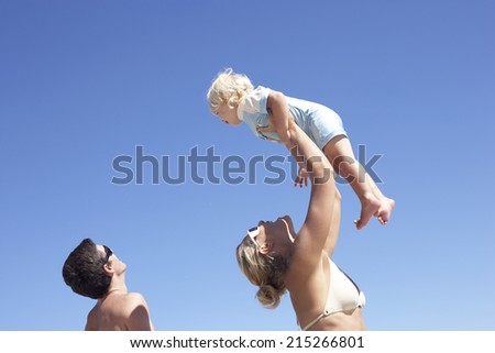 Two generation family standing on beach, mother lifting daughter (2-4) above head, profile