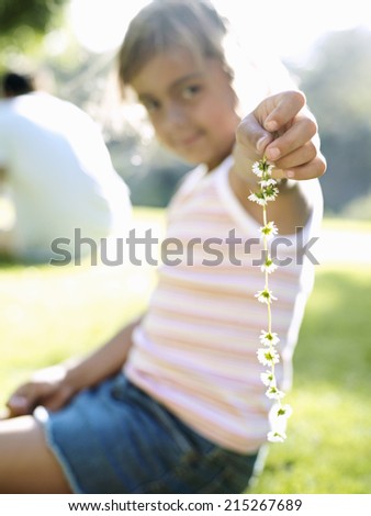 Girl (6-8) sitting on grass in park, holding daisy chain, smiling, portrait (differential focus)