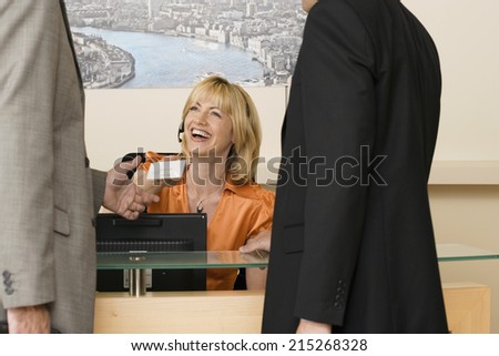 Receptionist working behind reception desk, receiving business card from businessman, smiling