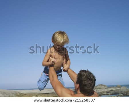 Father and son (4-6) playing on beach, man lifting boy above head
