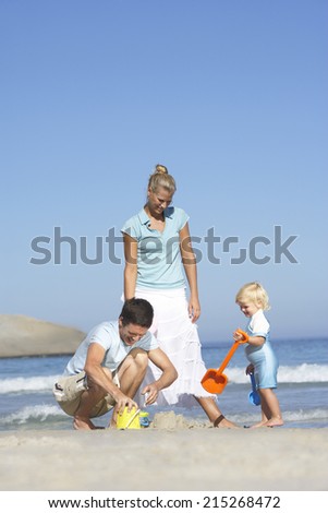 Two generation family playing with bucket and spade on sandy beach, sea in background