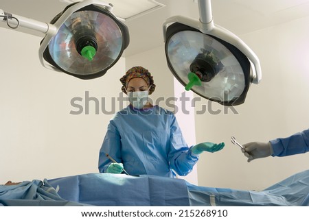 Surgeon in scrubs and surgical mask operating on patient, colleague passing scissors