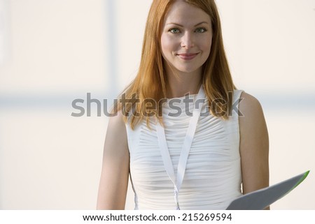 Woman in white sleeveless top holding folder, smiling, front view, portrait