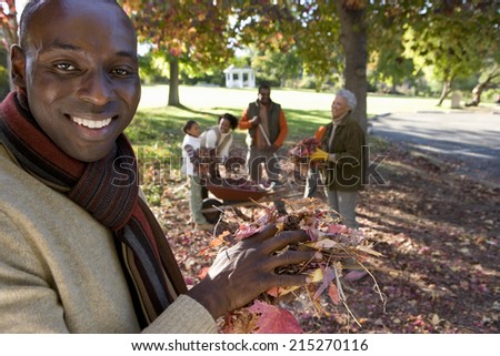 Multi-generational family collecting autumn leaves in garden, focus on father standing in foreground, portrait