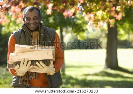Senior man collecting firewood in autumn park, smiling, front view, portrait