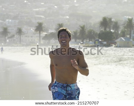 South Africa, Cape Town, man in swimming shorts jogging along sandy beach, smiling, front view