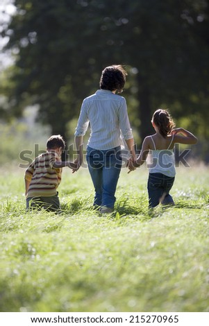 Mother walking hand in hand with son (6-8) and daughter in field, rear view