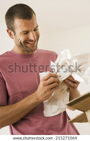 Man moving house, wrapping crockery in paper, smiling, close-up