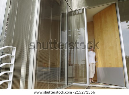 Senior woman standing in doorway at home, opening door, smiling, portrait