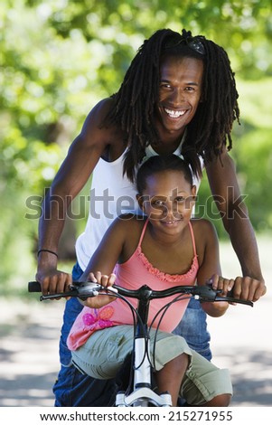 Father and daughter sitting on mountain bike, smiling, portrait