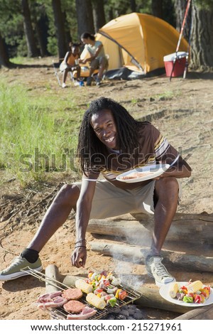 Family having lunch on camping trip, focus on man cooking food in foreground, smiling, portrait