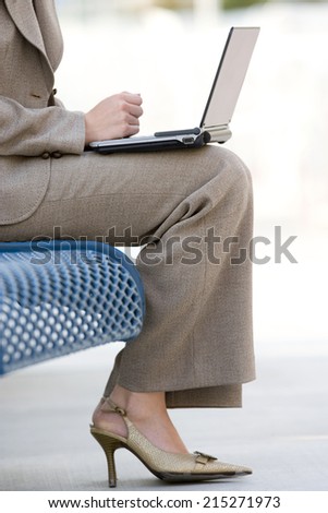 Businesswoman in suit and high heels using laptop on pavement bench, low section, profile