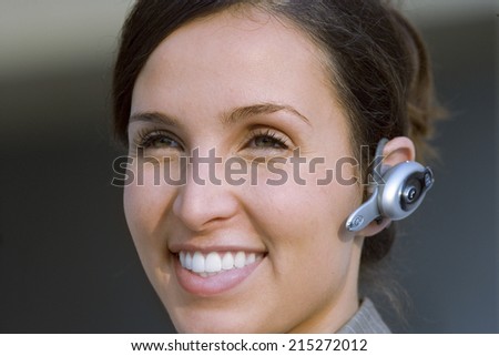 Businesswoman wearing mobile phone hands-free device, smiling, close-up