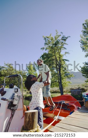 Father lifting son (8-10) onto moored motorboat beside lake jetty, smiling, side view