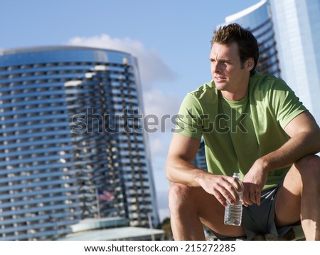 Man, in sportswear, sitting on bench, taking break from jogging in park, holding water bottle (tilt)