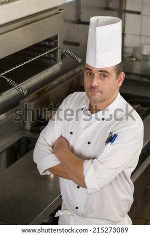 Male chef standing in commercial kitchen, arms folded, portrait, elevated view