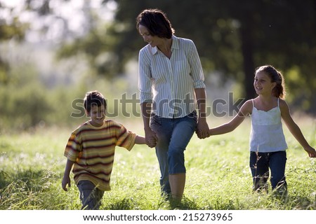 Mother walking hand in hand with son (6-8) and daughter in field, front view