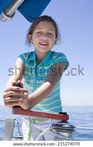 Girl (8-10) winding rope pulley of boat rigging on deck of sailing boat out at sea, smiling, front view, portrait