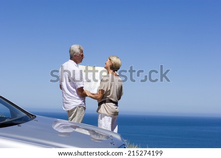 Senior couple standing beside parked car on clifftop overlooking Atlantic Ocean, consulting map, rear view
