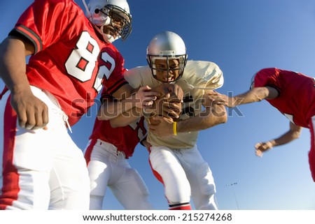 American football players tackling opposing player with ball, low angle view
