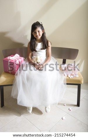 Girl (8-10), dressed in bridesmaid dress, sitting beside wedding gift on bench, smiling, front view, portrait