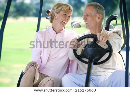 Mature couple sitting in golf buggy on golf course, man driving, smiling, front view